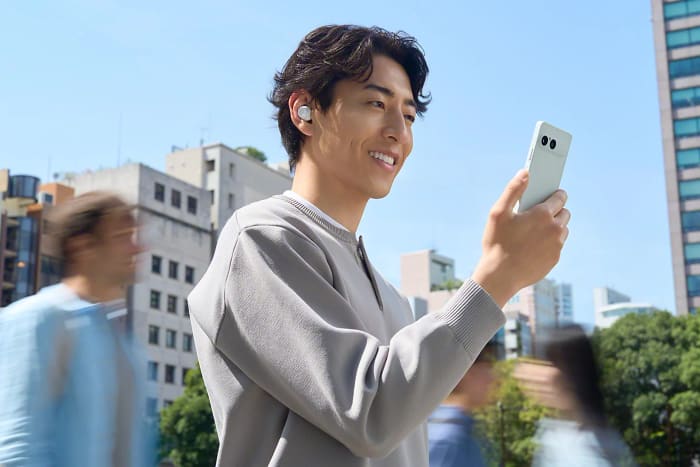 Person wearing earbuds and holding a Sony Xperia 10 VIII outdoors
